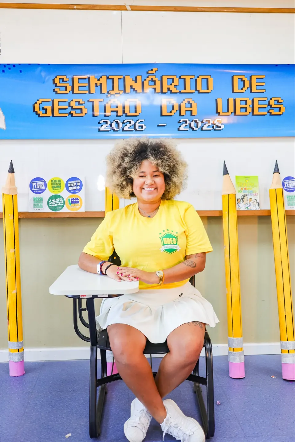 Estudante com a camiseta da UBES em frente a um painel do Seminário de Gestão da UBES
