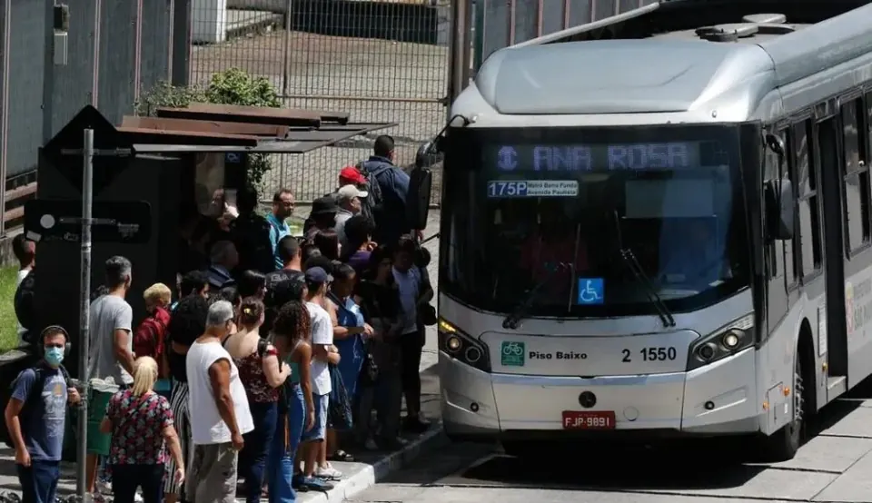 Fila de estudantes no ponto, ao lado de um ônibus