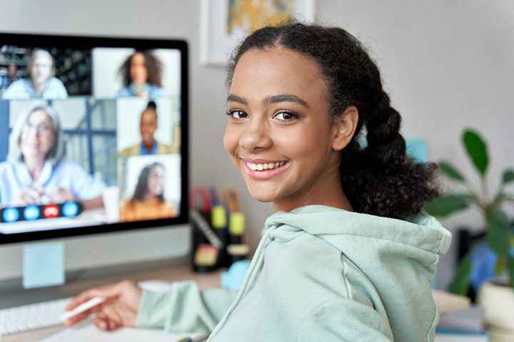 Uma estudante secundarista sorrindo enquanto assiste aula online.